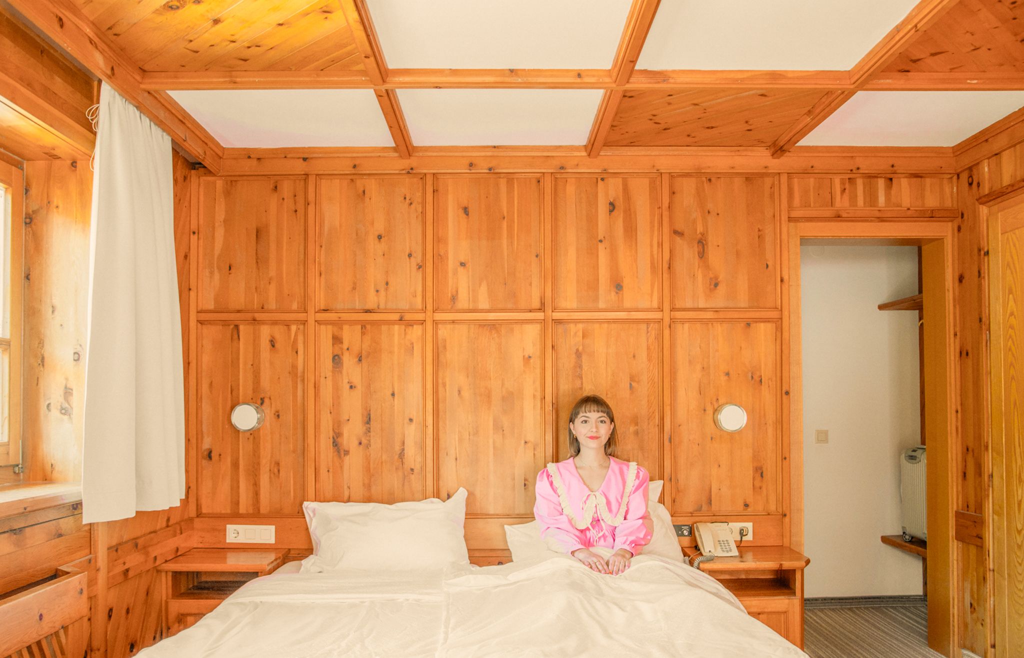 Ein Zimmer im Glemmtalerhof mit warmen Holzdetails und einer Frau auf dem Bett.