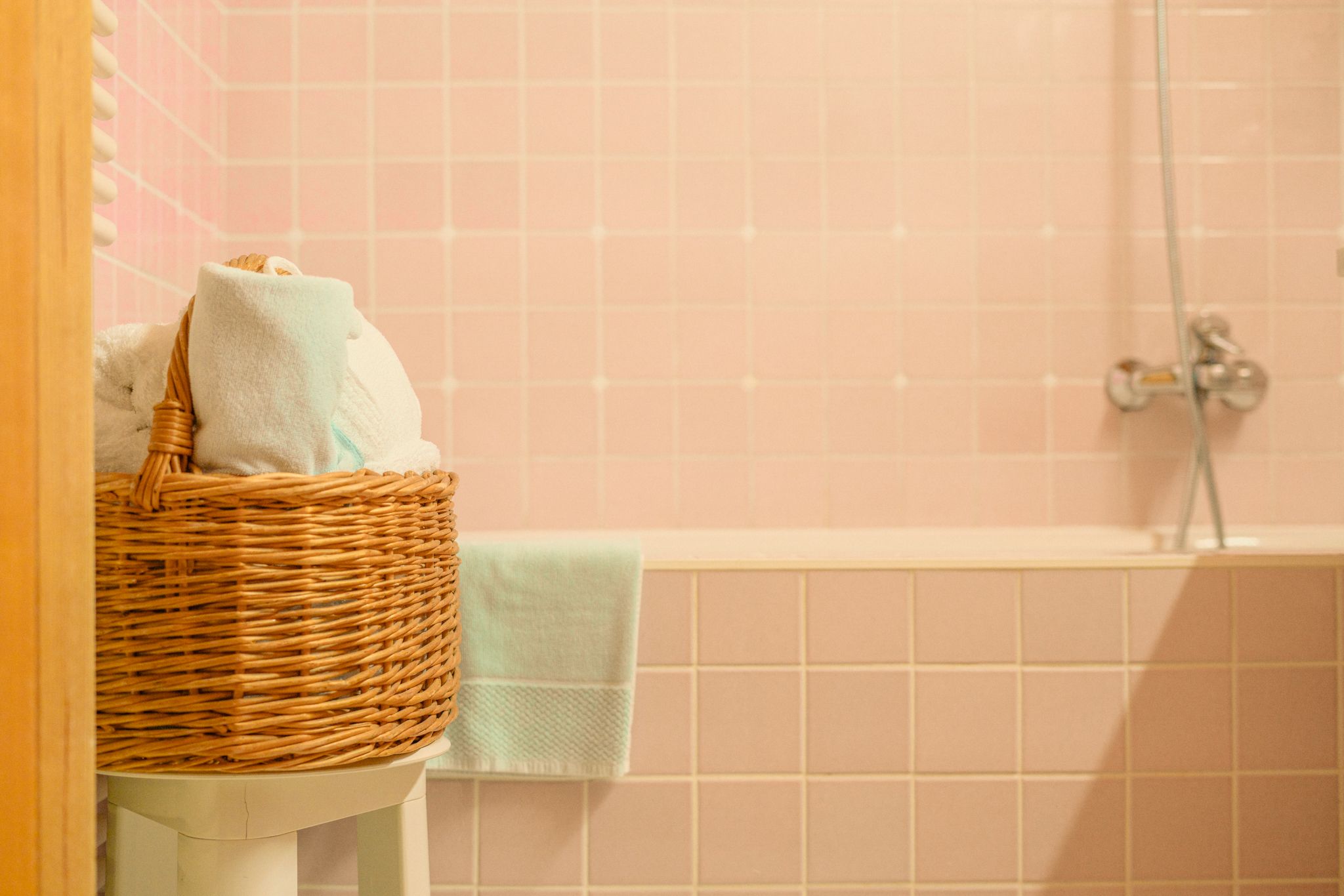 Ein gemütliches Badezimmer mit Handtüchern im Korb und sanften rosa Fliesen. DE