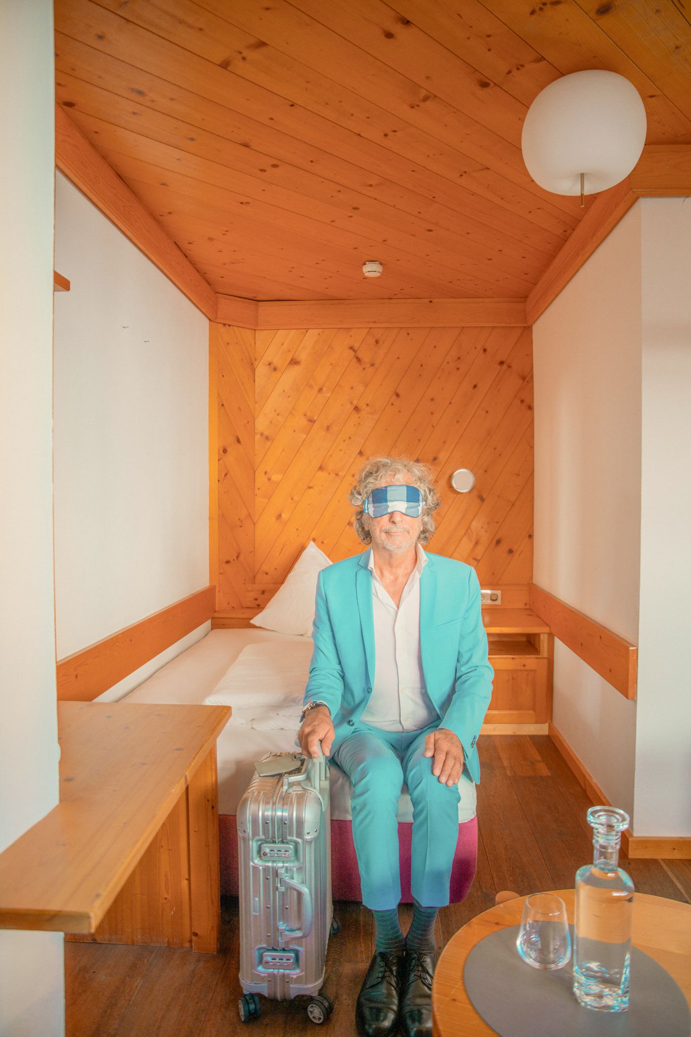 Ein Mann im blauen Anzug sitzt im Glemmtalerhof mit Koffer, bereit für Abenteuer.