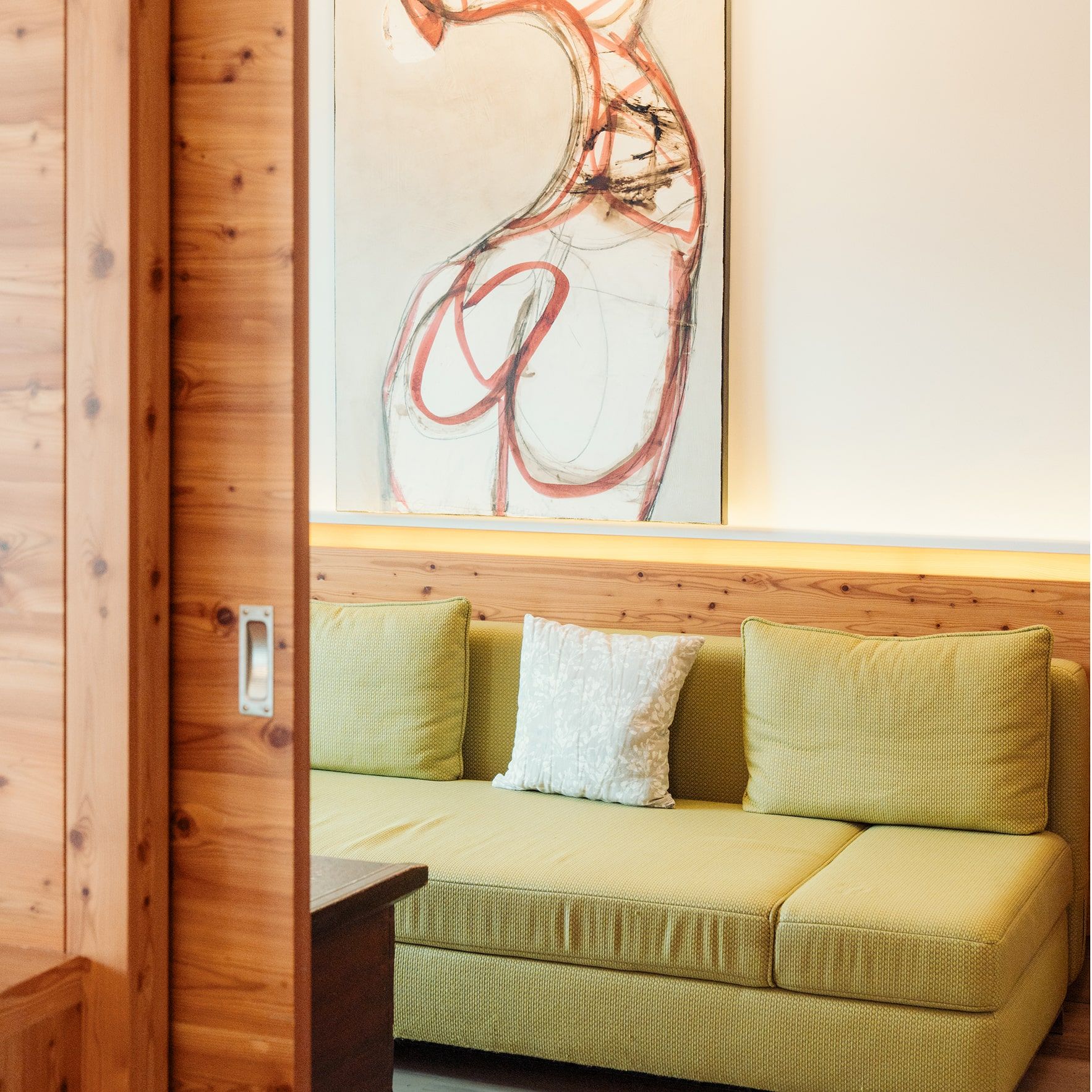 A cozy living space featuring a green couch, decorative pillows, and an abstract painting on the wall.