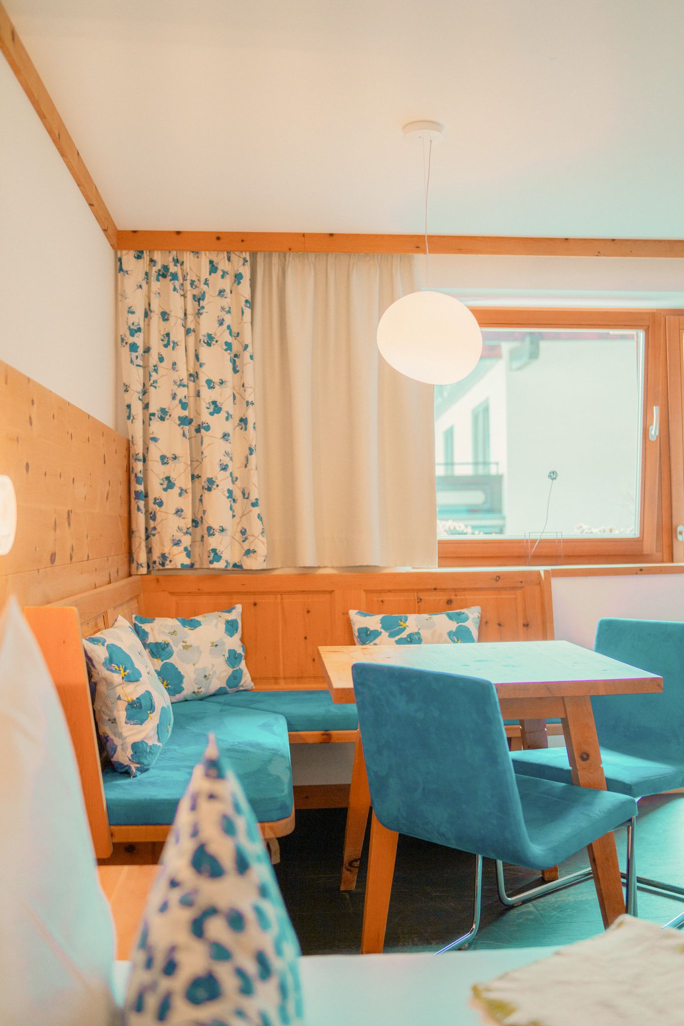 Gemütlicher Essbereich im Glemmtalerhof, modern eingerichtet mit blauen Akzenten und floralen Vorhängen.