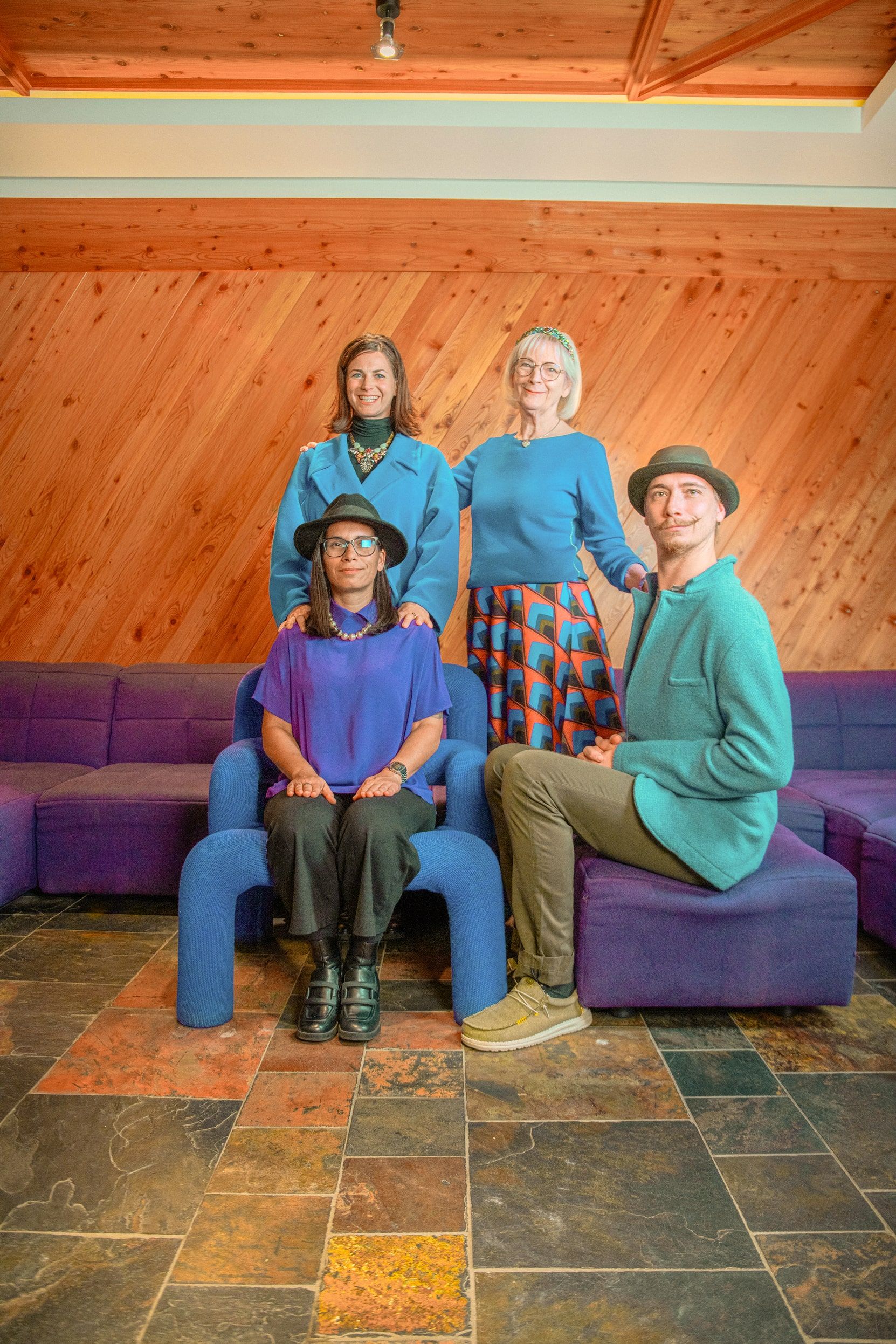 Vier Personen posieren in stylischen Outfits auf lila Sofas im Glemmtal, umgeben von einem rustikalen Holzinterieur.