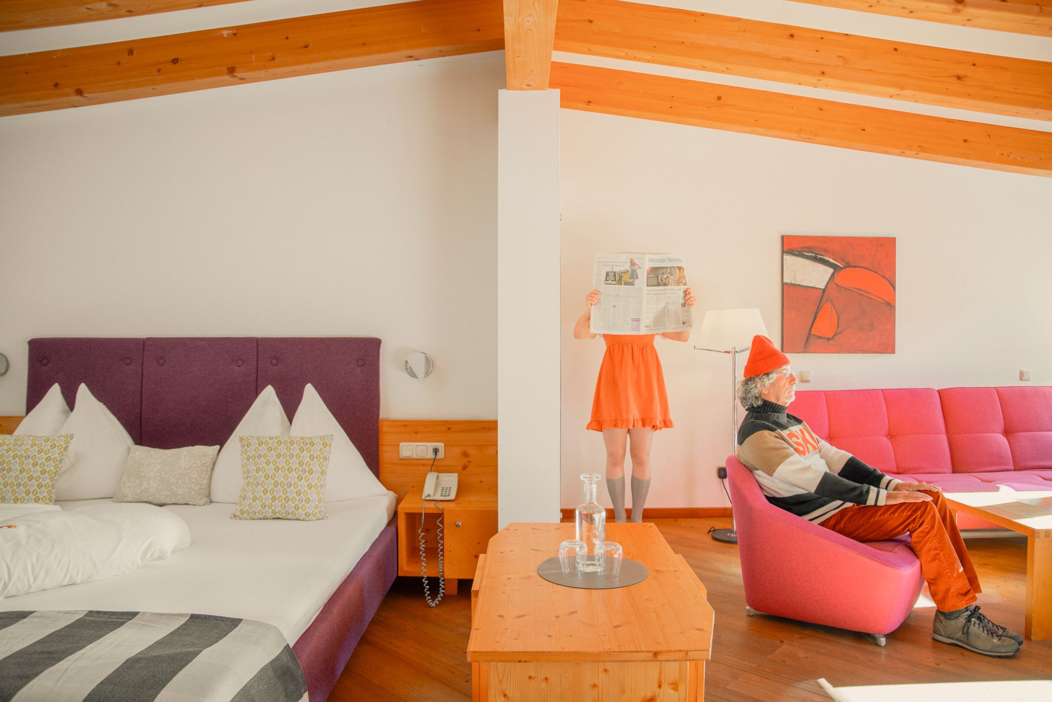 Glemmtalerhof in Hinterglemm, modernes Zimmer, lebendige Farben, Person mit Zeitung und jemand auf dem pinken Sofa.